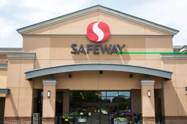 The front entrance of a Safeway grocery store with the company's logo prominently displayed above the main doors, showcasing the store's modern exterior design and hinting at the various financial services available, such as Safeway Money Order.